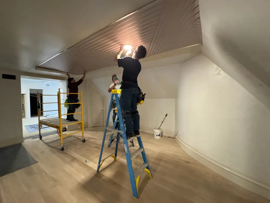 Two-installer commercial crew installing wood-slat wallcovering on a vaulted ceiling