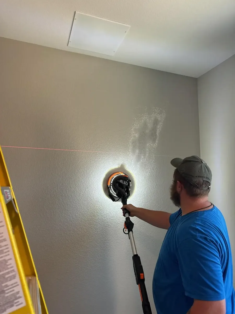Technician sanding a wall to a glass-smooth finish ahead of wallpaper installation